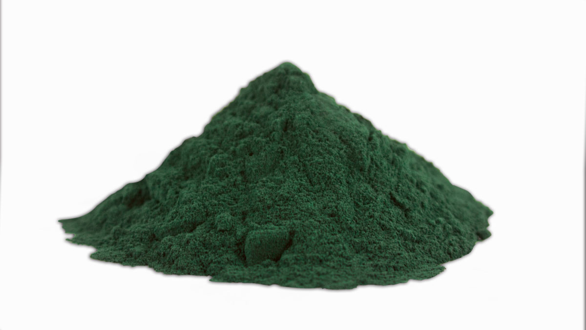 Hromádka tmavě zeleného prášku ze spiruliny na bílém pozadí