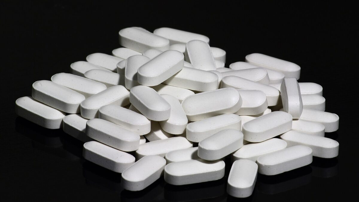 Hromádka bílých podlouhlých tablet vápníku s vitaminem D na černém pozadí