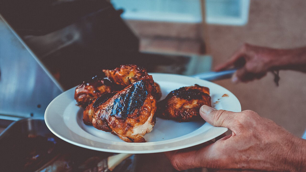 Ruka drží talíř s grilovaným kuřecím masem u grilu