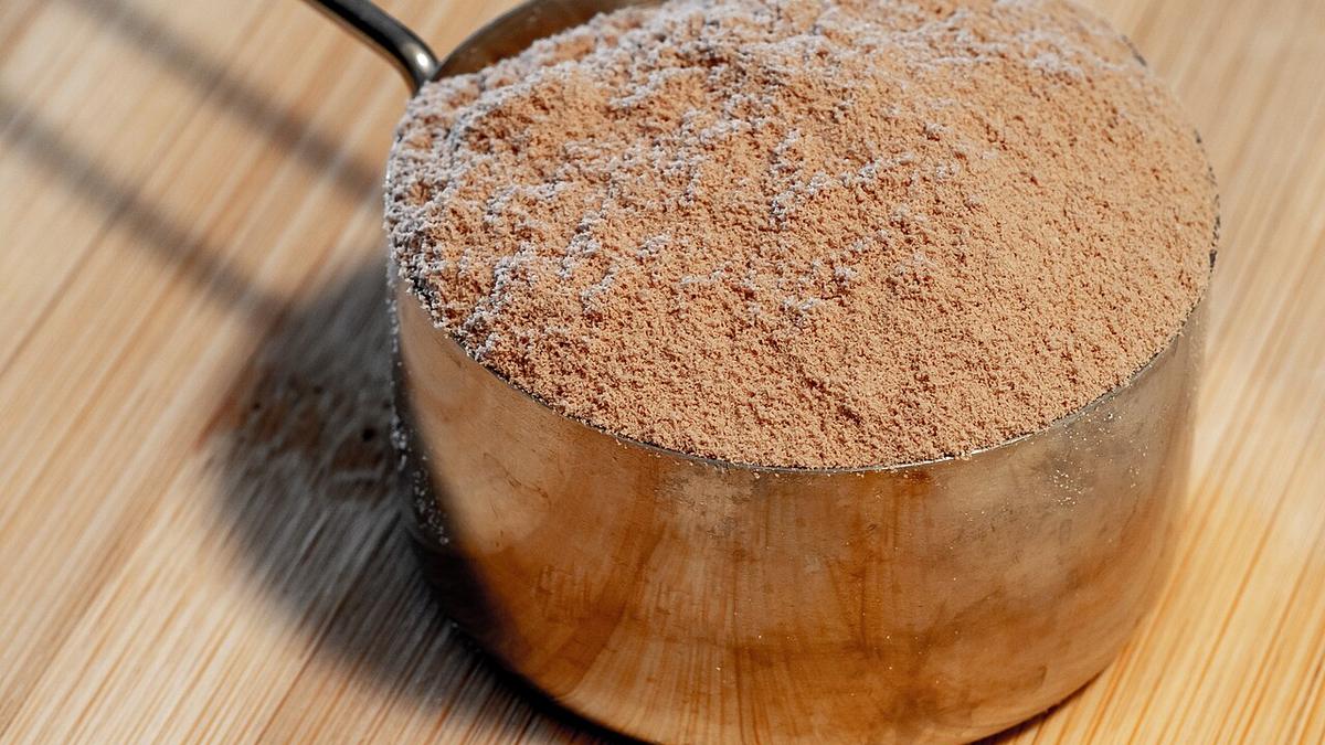 Kovová odměrka plná čokoládového proteinového prášku na dřevěné desce