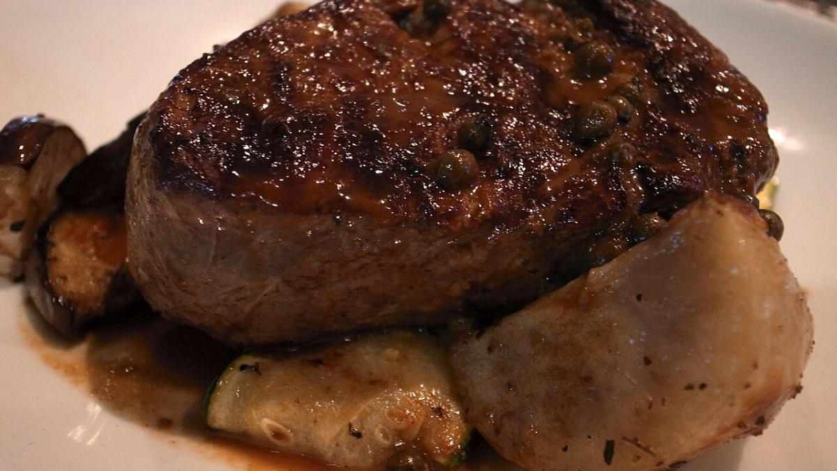 Hovězí steak s pečenými bramborami a cuketou na bílém talíři