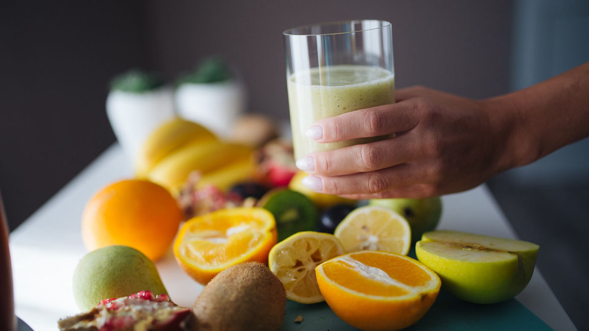 Ruka drží pohár smoothie medzi citrusmi a kiwi