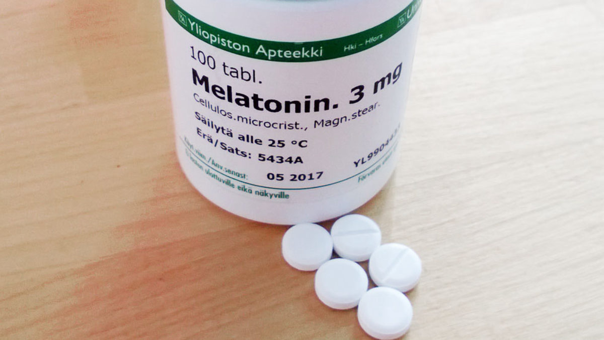 Lahvička melatoninu 3 mg z finské lékárny a pět bílých tablet na dřevěném stole