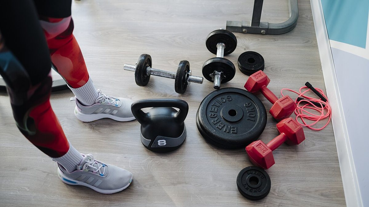 Jednoručky, kettlebell, kotúč a švihadlo na podlahe vedľa nôh v športovej obuvi