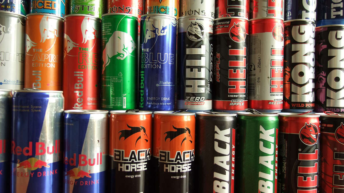 Regál plný plechovek energetických nápojů různých značek, mezi nimi Red Bull, Hell a Black Horse
