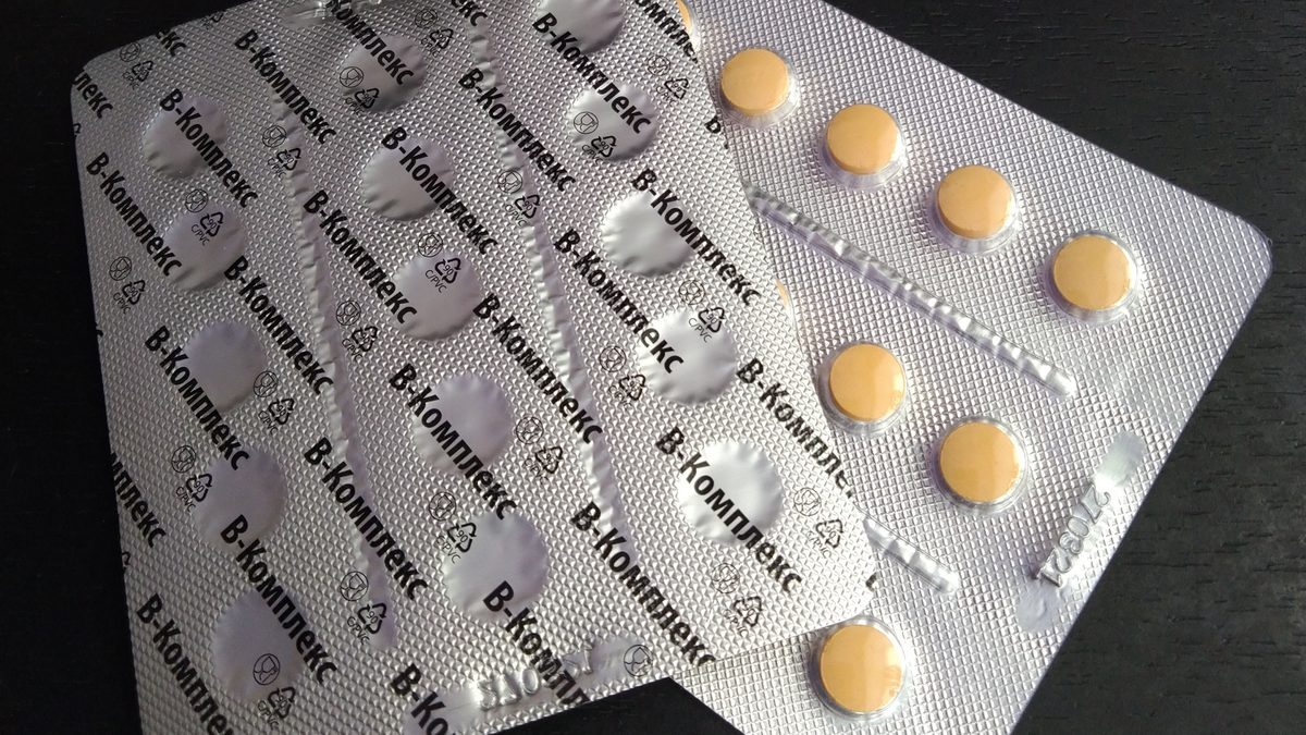 Blistry se žlutými tabletami B-komplexu na tmavém stole