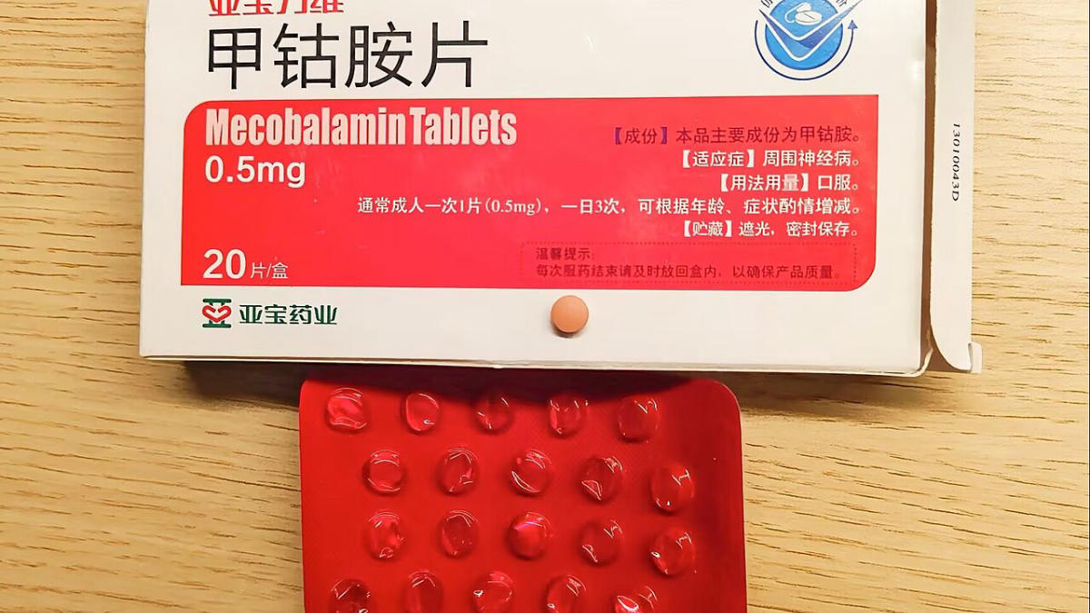 Krabička tablet methylkobalaminu s blistrem červených tablet na dřevěném stole