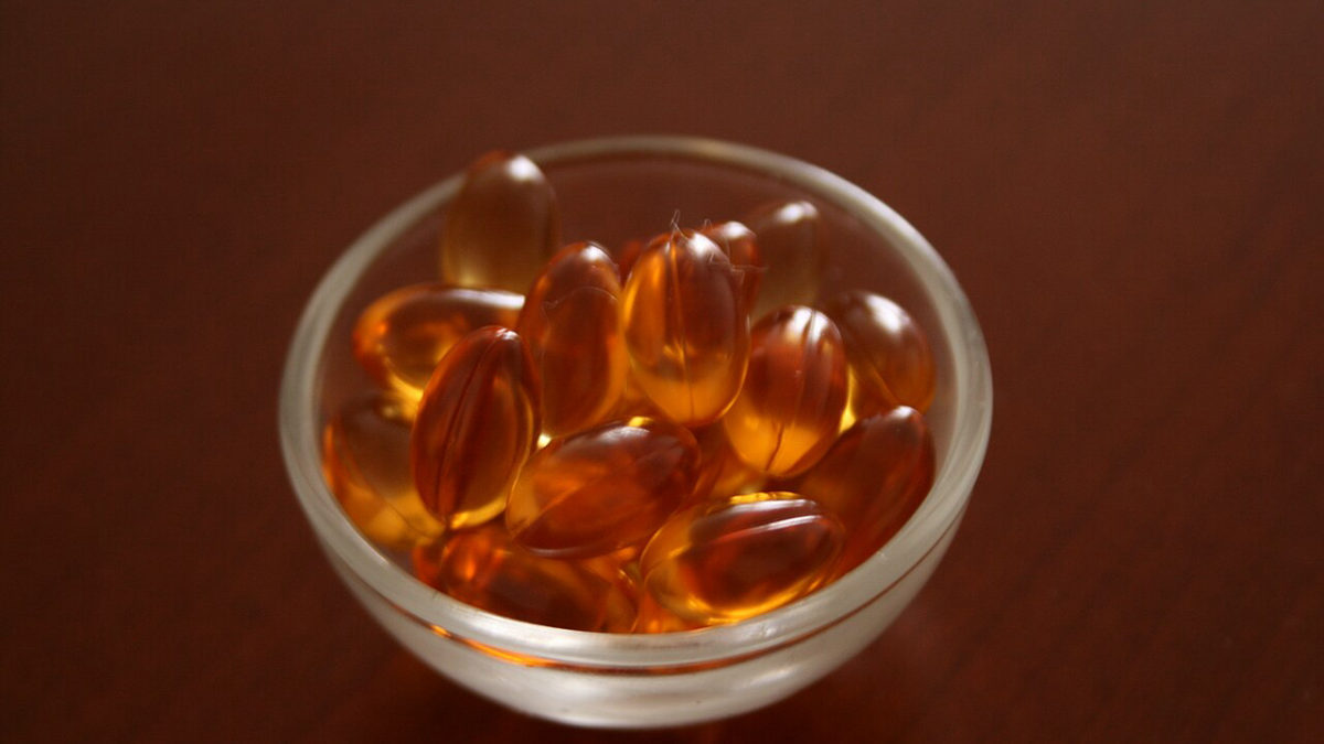 Průsvitné oranžové tobolky vitaminu E ve skleněné misce na tmavém dřevě